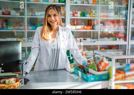 Attraktive Apothekerin in Uniform, die in der Apotheke vor der Kamera lächelt Stockfoto