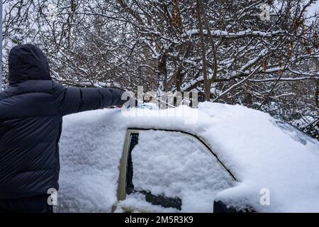 Breslau, Polen - 20. Dezember 2022: Ein Mann, der im Winter Schnee vom Autodach reinigt. Alter Mercedes Benz 190D. Stockfoto