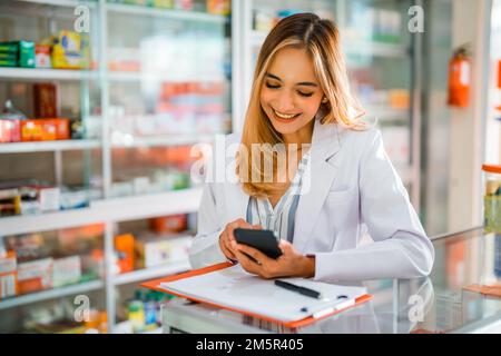 Asiatische Apothekerin mit Handy während der Arbeit in der Apotheke Stockfoto