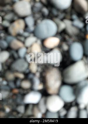 Schließen. Verwischen Sie Fotos oder Unschärfe-Effekte abstrakter Hintergründe von glatten kleinen Felsen auf schwarzem Sand. Für Tapeten Stockfoto