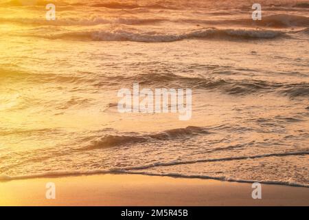 Sonnenuntergang über dem Meer. Riplpe Meerwasseroberfläche mit kleinen Wellen. Ozeanwasser Schaum Spritzwasser Sandstrand Stockfoto