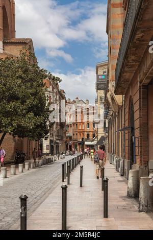 Fußgänger gehen entlang der gepflasterten Straße Rue des Arts, die von historischen Backsteinhäusern gesäumt ist, Toulouse, Haute-Garonne, Frankreich Stockfoto