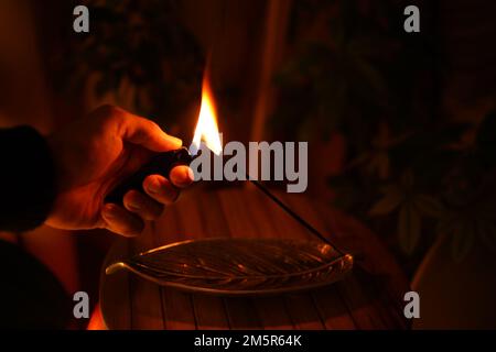 Einen Joss Stick in einem warmen, hellen Meditationsraum anzünden Stockfoto