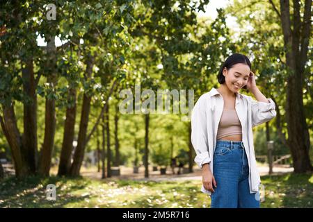 Bild von koreanischen Mädchen zu Fuß im Park, lächelnd, während mit einem achtsamen Spaziergang im Wald Stockfoto