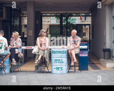 Bukarest, Rumänien - August 2022: Urbane Szene mit einem Paar mittleren Alters, das an einem Tisch sitzt und ein Bier in der Altstadt von Buchares trinkt. Stockfoto