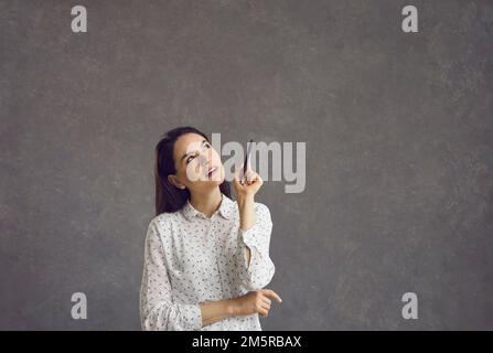 Eine Frau, die einen Stift hält, wegschaut, über eine interessante Idee nachdenkt und sich etwas vorstellt Stockfoto