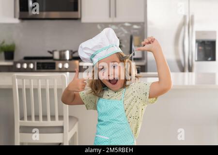 Der Kinderkoch bereitet Speisen in der Küche zu. Kinder kochen. Teenager Junge mit Schürze und Chefhut bereitet eine gesunde Mahlzeit zu. Stockfoto