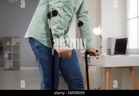 Der junge Mann lehnt sich an Krücken und versucht, nach der Rehabilitation zu Hause in sein Wohnzimmer zu gehen. Stockfoto