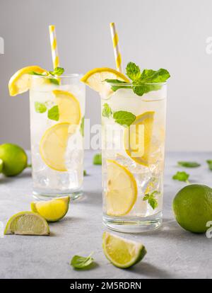 Mineralwasser mit frischen Zitronen. Erfrischendes Getränk mit Limette, Zitrone, Minze und Eis in einem großen Glas auf grauem Hintergrund. Sommerkonzept mit kalten Getränken. Fro Stockfoto