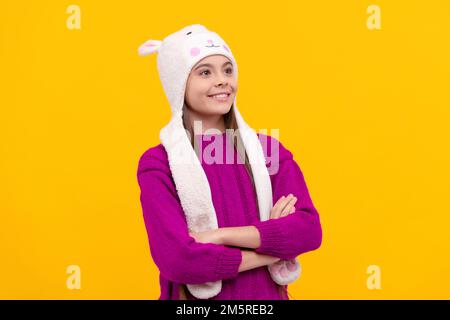 drücken Sie positive Emotionen aus. Glückliches Kind mit Ohrenschützenmütze. Das Kind trägt warme Kleidung auf gelbem Hintergrund. Wintermode und -Schönheit für Kinder. Teenager in Strick Stockfoto