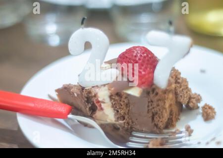 Geburtstagskuchen mit Kerzen in der Form von Nummer 27 auf einem Tisch für ein paar Leute und eine Flasche Wein im Hintergrund, Erwachsenentarif-Konzept Stockfoto