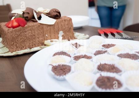 Geburtstagskuchen mit Kerzen in der Form von Nummer 27 auf einem Tisch für ein paar Leute und eine Flasche Wein im Hintergrund, Erwachsenentarif-Konzept Stockfoto