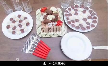 Geburtstagskuchen mit Kerzen in der Form von Nummer 27 auf einem Tisch für ein paar Leute und eine Flasche Wein im Hintergrund, Erwachsenentarif-Konzept Stockfoto