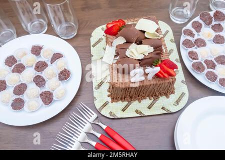 Geburtstagskuchen mit Kerzen in der Form von Nummer 27 auf einem Tisch für ein paar Leute und eine Flasche Wein im Hintergrund, Erwachsenentarif-Konzept Stockfoto