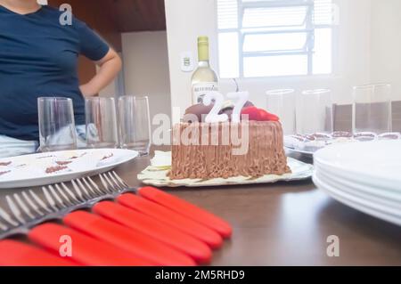 Geburtstagskuchen mit Kerzen in der Form von Nummer 27 auf einem Tisch für ein paar Leute und eine Flasche Wein im Hintergrund, Erwachsenentarif-Konzept Stockfoto