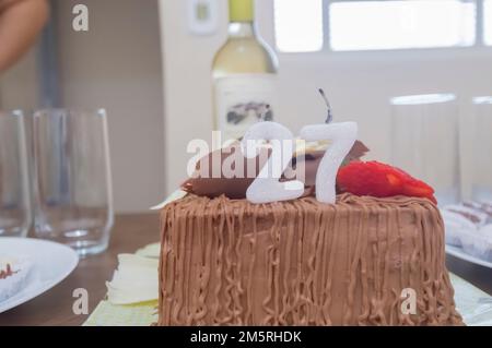 Geburtstagskuchen mit Kerzen in der Form von Nummer 27 auf einem Tisch für ein paar Leute und eine Flasche Wein im Hintergrund, Erwachsenentarif-Konzept Stockfoto
