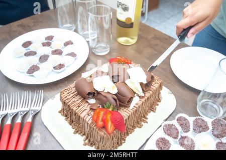 Geburtstagskuchen mit Kerzen in der Form von Nummer 27 auf einem Tisch für ein paar Leute und eine Flasche Wein im Hintergrund, Erwachsenentarif-Konzept Stockfoto