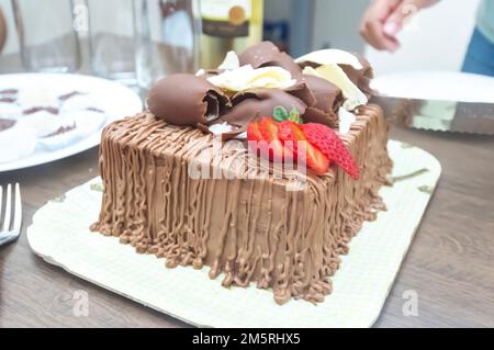 Geburtstagskuchen mit Kerzen in der Form von Nummer 27 auf einem Tisch für ein paar Leute und eine Flasche Wein im Hintergrund, Erwachsenentarif-Konzept Stockfoto