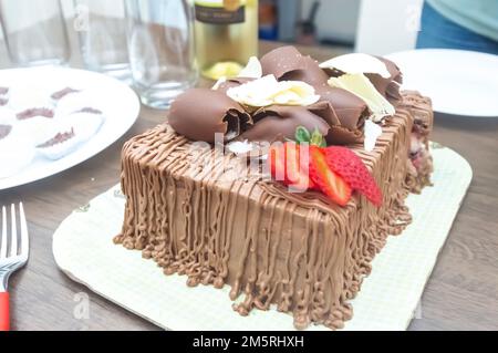 Geburtstagskuchen mit Kerzen in der Form von Nummer 27 auf einem Tisch für ein paar Leute und eine Flasche Wein im Hintergrund, Erwachsenentarif-Konzept Stockfoto