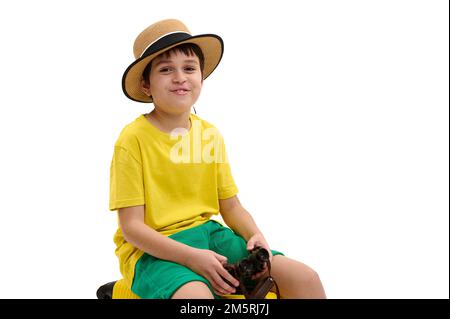 Ein lächelnder Reisender, trägt einen Strohhut und gelb-grüne Sommerkleidung, hält ein Fernglas und lächelt vor der Kamera auf Weiß Stockfoto