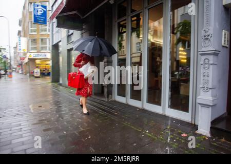 30-05-2016 Köln, Deutschland. Eine Frau mit einer leuchtend roten Tasche läuft mit einem Regenschirm vom Regen auf der Kölner Straße Stockfoto