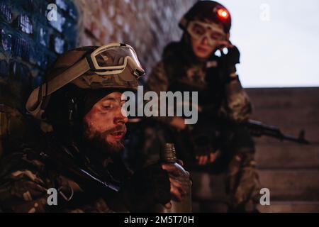 Waffenbrüder, die vor dem Hintergrund der ukrainischen Flagge ruhten. Das ukrainische Militär im einstürzten Gebäude, das sich aus dem Krieg erholt hat. Stockfoto