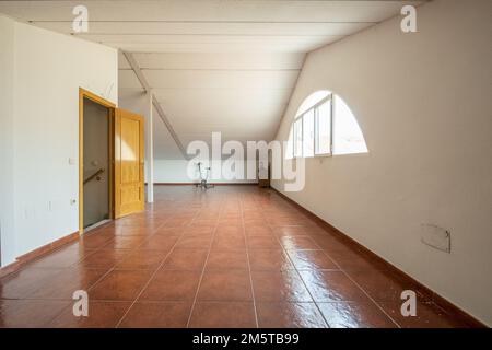 Ein großer leerer Flur eines Einzelhauses auf dem Dachboden mit Fenstern, die fast halbrunden Formen haben, mit Eichentür zum Treppenwechsel Stockfoto