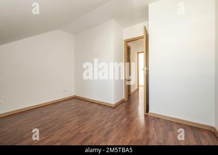 Ein Zimmer auf dem Dachboden mit schrägen Decken, Zugangstüren zu anderen Zimmern und dunklen Laminatböden Stockfoto