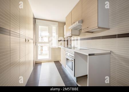 Neu ausgestattete Küche mit Holzmöbeln und Geräten, die integriert werden müssen, und Ausgang zu einer Terrasse mit einer weißen Aluminium- und Glastür Stockfoto