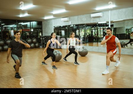 Eine Gruppe sportlicher Männer und Frauen, die mit einem Lehrer Squats machen Stockfoto