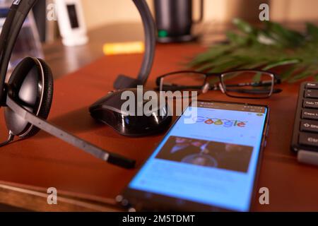 Arbeiten Sie mit den Kopfhörern und der Maus zu Hause neben Nachrichten über Mobiltelefone und Kaffeetassen Stockfoto
