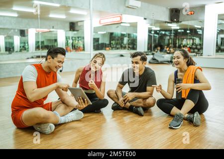 Gruppe junger asiatischer Athleten, die sich unterhalten und ein Tablet benutzen Stockfoto