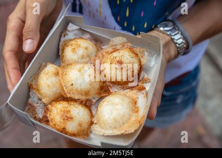 Eine Schachtel Khanom Khrok oder Kokosnuss-Reis-Pfannkuchen, traditionelles thailändisches Dessert mit Kokosmilch und Reisblumen. Nationale Küche Thailands. Stockfoto