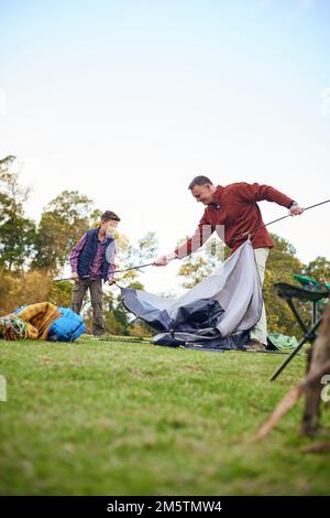 Er ist ein großartiger kleiner Helfer. Ein Vater und ein Sohn, die zusammen ein Zelt aufstellen, während sie campen. Stockfoto