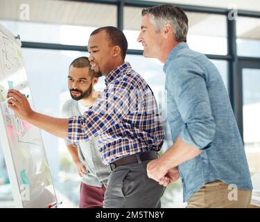 Große Köpfe machen die Arbeit einfach. Drei Geschäftsleute, die an einem Whiteboard arbeiten. Stockfoto