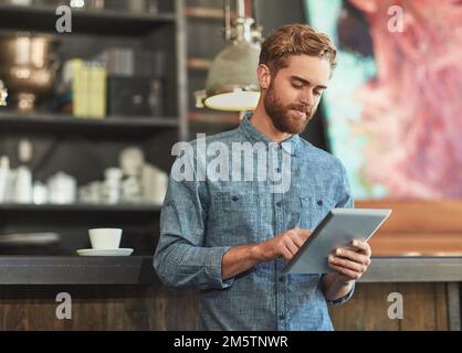 Ein kleines Unternehmen zu besitzen Drahtlose Technik ist die richtige Wahl. Ein junger Mann, der ein digitales Tablet in einem Café benutzt. Stockfoto