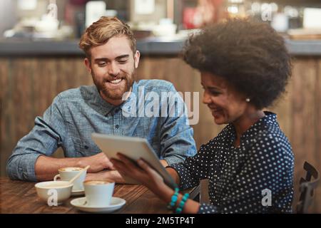 Diese App ist genau das, was wir brauchen. Ein junges Paar, das ein digitales Tablet zusammen auf einem Kaffeeabend benutzt. Stockfoto