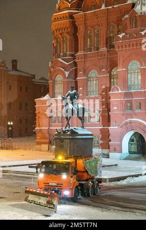 Moskau, Russland - 7. Dezember 2022: Das Auto KAMAZ räumt in einer kalten Winternacht Schnee von der Straße in der Nähe des Kremls und des Roten Platzes. Zhukov-Gedächtnisstatu Stockfoto