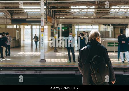 Älterer Mann, der auf die Ankunft des Zuges am Bahnhof in Tokio wartet Stockfoto