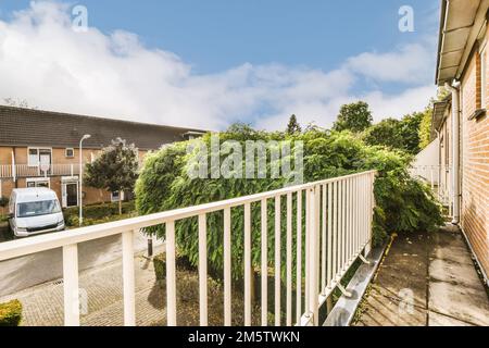 Die Außenseite eines Hauses mit Bäumen und Büschen, die an der Seite des Hauses wachsen, davor ist ein weißer Zaun Stockfoto