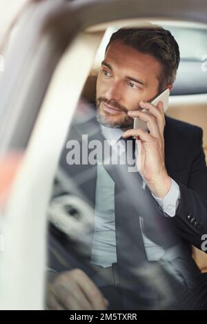 Ich bin fünf Minuten vom Büro entfernt. Ein Geschäftsmann, der sein Handy benutzt, während er im Auto unterwegs ist. Stockfoto