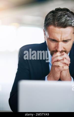 Ich hoffe auf ein positives Ergebnis. Ein besorgter Geschäftsmann, der sich seinen Laptop ansieht, mit Beunruhigung im Büro. Stockfoto