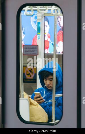 Ein junger Passagier, der im Zug Musik auf seinem Handy hört Stockfoto