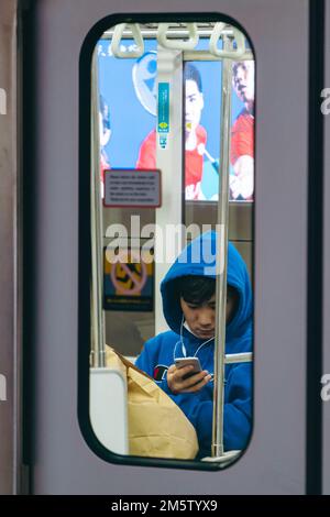 Ein junger Passagier, der im Zug Musik auf seinem Handy hört Stockfoto