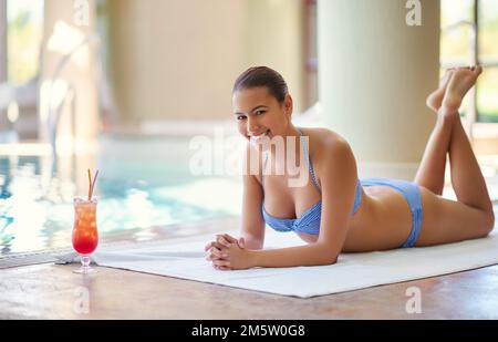 Das Leben ist cool am Pool. Eine attraktive junge Frau, die einen Drink am Pool genießt. Stockfoto