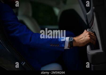 Ein Mann im blauen Anzug öffnet die Autotür. Nahaufnahme eines Mannes Hand mit einer teuren Uhr. Stockfoto