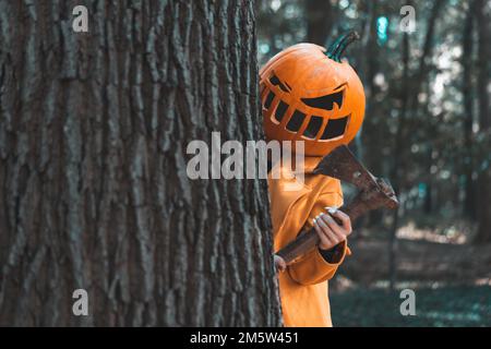 Eine Nahaufnahme einer Frau, die einen Kürbis auf dem Kopf trägt und eine Axt im Wald hält Stockfoto