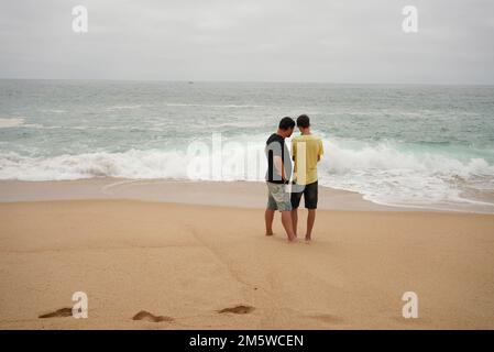 Vater und Sohn stehen und schauen die Wellen am Strand an Stockfoto