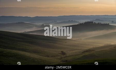 Hügelige Landschaft mit nebiger Atmosphäre und Landsitz, Sonnenaufgang, Kreta Senesi, Provinz Siena, Toskana, Italien Stockfoto