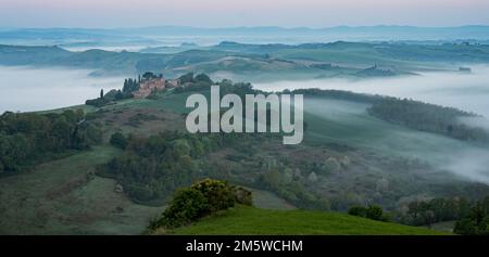 Hügelige Landschaft mit nebiger Atmosphäre und Landsitz, Sonnenaufgang, Kreta Senesi, Provinz Siena, Toskana, Italien Stockfoto